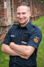 Portrait eines Justizvollzugsbeamten, der lächelt und die Arme vor der Brust verschränkt hat