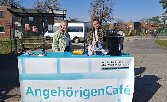 zwei Mitarbeiterinnen unter freien Himmel hinter einem Tisch mit dem Banner des Cafés