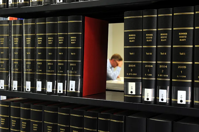 Reihe an Gesetzesbüchern, durch eine Lücke sieht man einen Mann über ein Buch gebeugt