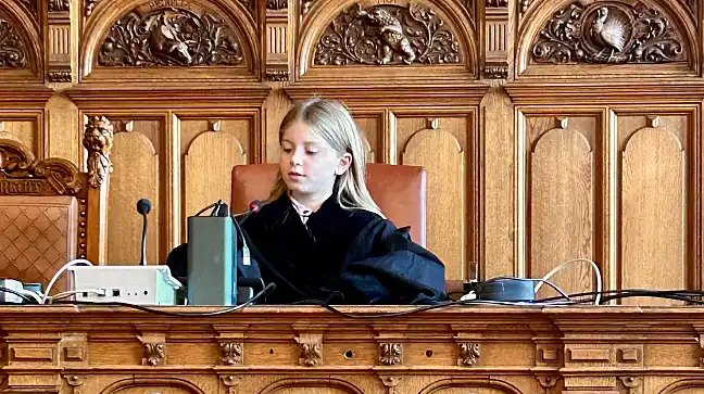 Kind sitzt in einer Robe auf einer Richterbank und bedient das Mikrofon