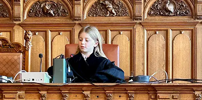 Kind sitzt in einer Robe auf einer Richterbank und bedient das Mikrofon